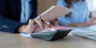 Focused Financial Analysis. Close-up of a hand using a calculator while discussing financial documents. photo