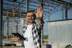 Giving orders by the hand. Senior worker is near the unfinished greenhouse, working photo
