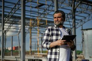 Wireless device, holding digital tablet ,,,in, hands. Senior worker is near the unfinished greenhouse, working photo