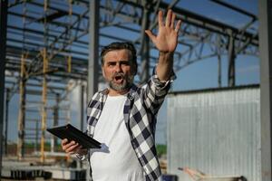Giving orders ,,by the hand. Senior, worker is near the unfinished greenhouse, working photo