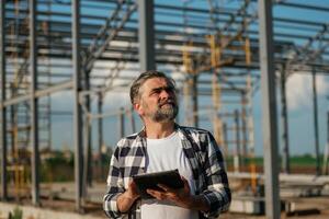 Serious facia,,l expression. Senior worker is near the unfinished greenhouse, working photo