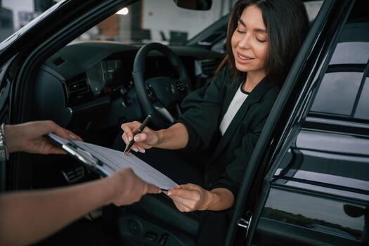 Writing by a pen., Process of buying new car, woman is signing documents while sitting in a new automobile photo