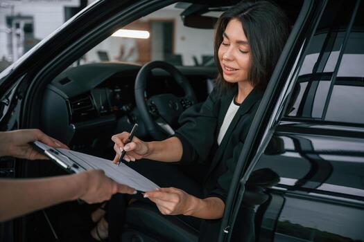 Writing by ,,a pen. Process of buying new car, woman is signing documents while sitting in a new automobile photo