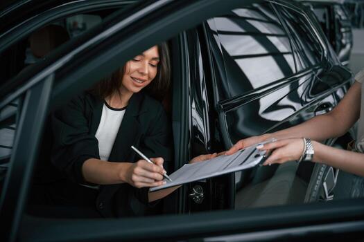 Writing by ,a ,pen. Process of buying, new, car, woman is signing documents while sitting in a new automobile photo