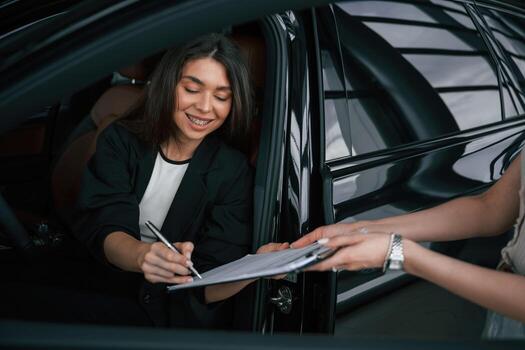 Writing by a pen. Process, of ,buying new car, woman is signing documents while sitting in a new automobile photo