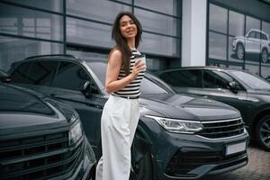 Holding,, cup of coffee. Attractive young woman is outdoors near her brand new car photo