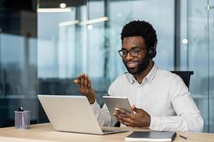 Support service worker at workplace with headset phone and tablet computer in hands. Man consults customers remotely using call. Business meeting conference remotely. photo