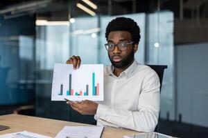 A professional man presents financial data with a graph during a meeting in the office. The analysis is shown with data bars on paper. photo