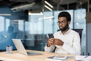 Serious focused man using app on phone. Businessman thinking sitting at desk in middle of office, typing text message on smartphone, and browsing online internet pages. photo