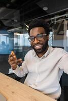 A smiling man in glasses is gesturing, likely in a call, showcasing enthusiasm in a modern office setting photo