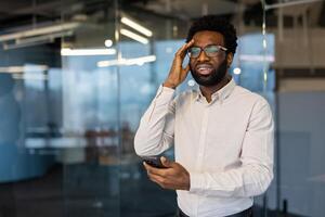 An african-american man reacts with dismay after reading a message on his mobile phone inside an office setting photo