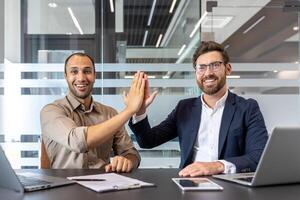 Two diverse business professionals are celebrating success with a high-five gesture in a modern office setting, smiling. photo