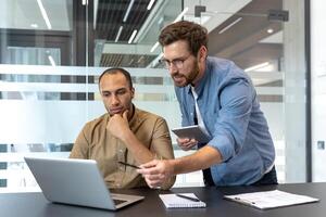 Two colleagues collaborate in a modern office setting, discussing information displayed on a laptop screen with focus and intent. photo