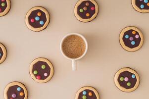 Trendy pattern composition made of colorful cookies with cup of coffee on pastel cream background. Minimal coffee with biscuits concept. Yummy sweet food and hot drink idea. Flat lay style. Top view. photo