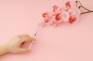 Hand injecting pink liquid into orchid flower with syringe on pastel pink background. Minimal surreal bloom concept. Trendy nature and science idea backdrop. Flat lay style. Top view banner. photo