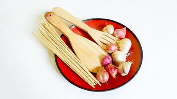 wooden spatula skewers, and shallots and garlic in a red plastic plate with white background. photo