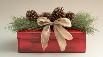A thoughtfully arranged red gift box adorned with a natural ribbon and pine cones rests gracefully on a neutral background for the holiday season photo
