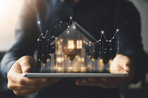 Businessman showcases digital house model on tablet, illustrating real estate investment growth with rising graphs in modern office setting photo