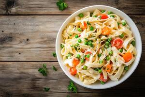 Delicious elbow pasta salad with carrots, onions, tomatoes, and peas in mayonnaise dressing served in a white bowl on wooden table photo