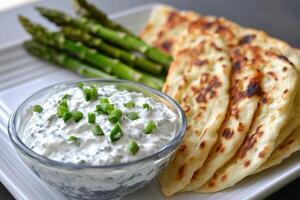 Delicious grilled asparagus served with creamy tzatziki and warm flatbreads on a plate in a casual dining setting photo