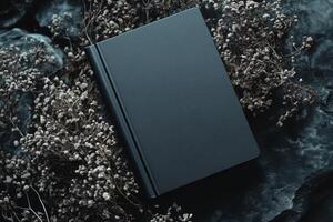 Stylish black book mockup with dark aesthetic placed among dried flowers on textured surface for design presentation photo