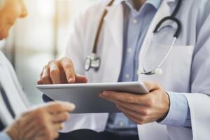 Young doctor consults with older patient using a digital tablet in a modern healthcare setting during a routine check-up photo