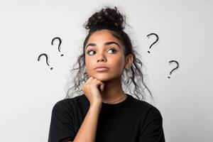 Young woman contemplating an idea with question marks around her in a thoughtful pose against a white background photo
