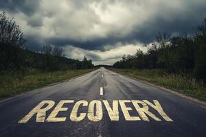 An empty road stretches into the distance, featuring the word 'RECOVERY' painted on the pavement beneath an overcast sky photo