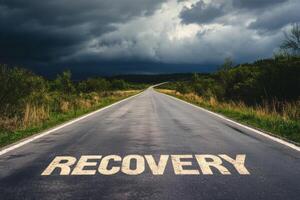 An empty road marked with the word recovery stretches into the horizon under an overcast sky photo