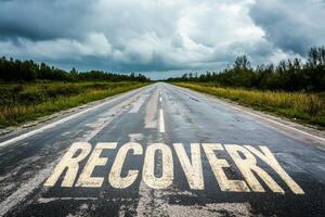 An empty road stretches into the distance with the word Recovery painted on it under an overcast sky, conveying a hopeful atmosphere photo
