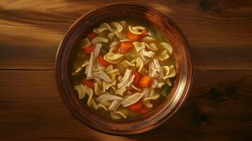 Warm bowl of chicken noodle soup with vegetables served on a wooden table in cozy evening lighting photo