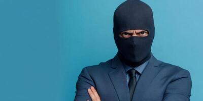 Professional man wearing a ski mask poses confidently in front of a blue background during a photoshoot in urban setting photo