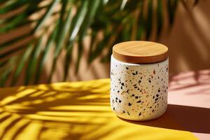 A ceramic storage container with a wooden lid, featuring a speckled design, sits on a yellow and peach backdrop with palm frond shadows photo