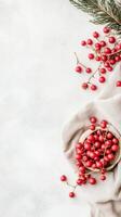 Red berries in bowl. Pine branch rests near cloth. White textured backdrop displays gardening elements on right side. Copy space on left. photo