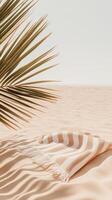Palm leaf casts shadow on light sand. Striped towel rests softly. Peaceful sandy landscape. Minimalist summer design with neutral tones. Tranquil beach scene. photo