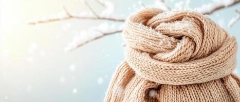 Winter season. Beige knitted scarf with snow on blurred twig branches and soft light blue background. Warm winter clothing closeup. photo