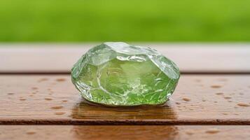 Green crystal stone rests on wood surface with raindrops, grass background, translucent gem, decorative item, nature object, mineral sample, close up photo