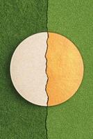 Circle shape split between beige and gold on green grassy ground. Vertical crack crossing the scene. Divided abstract concept with textured materials. photo