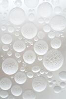 Glassy spheres and smaller drops on a light surface, many different sizes, close up, textured appearance, round shapes, abstract design, light gray backdrop. photo