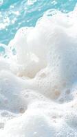 Ocean water foam rises above sand. White sea bubbles texture. Turquoise water sparkles in sunlight near beach. photo