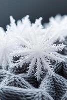 White snowflakes rest on gray knitted fabric. Close up view of winter design element with frosty texture. Christmas decoration on warm textile surface. photo
