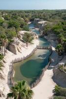 Tropical waterway flows amid white sand cliffs. Clear turquoise water meets lush green jungle. Wooden posts line the shore in the sun. Aerial view of exotic landscape. photo
