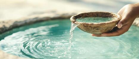 Hand holds stone bowl. Fresh water pours into pool. Light reflects on water. Calm nature setting. Focus on flow. photo