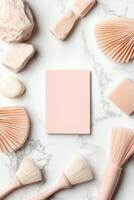 Flat lay arrangement. Pink blank card surrounded by stones, fans, brushes and soap on white marble background. Top view of objects in neutral tones. photo