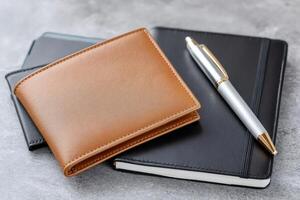 Leather wallet, notebook and pen resting on a gray desk photo