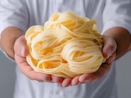 Fresh fettuccine pasta held by hands against simple background photo