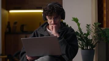 Concentrated Caucasian guy working laptop at home man freelancer programmer chatting website designer in headphones typing online application hipster developer using computer male playing virtual game video