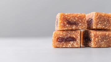 A close-up shot shows four delicious golden-brown squares of homemade oat and fruit granola bars stacked neatly on a light gray surface against a muted gray background. photo