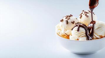 Creamy vanilla ice cream scoops in a white bowl being drizzled with rich chocolate sauce and chocolate shavings on a light gray background. photo