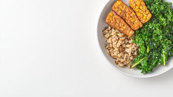 A healthy and delicious meal featu pan-fried tempeh, brown rice, and sauteed kale in a simple white bowl on a bright white background perfect for a vegetarian or vegan diet. photo
